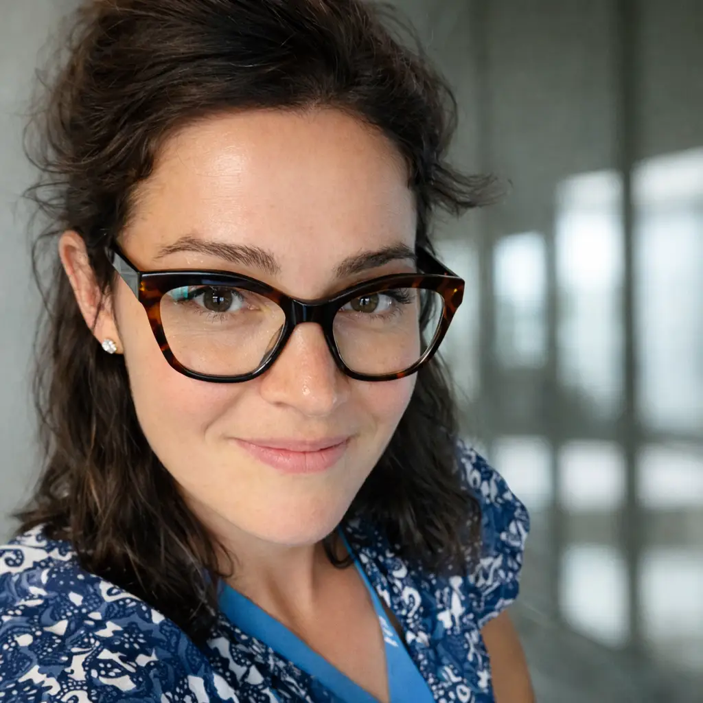 Portrait of a freelance interior and spatial designer wearing glasses, smiling in a softly lit studio setting.